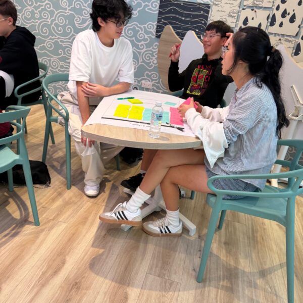 Three people collaborating around a table with sticky notes during a brainstorming session at Youth leadership camp