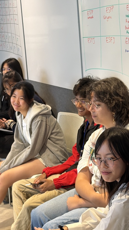 A group of young people sitting in a row and smiling in a room with whiteboards