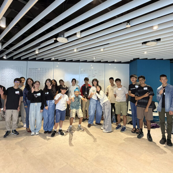 A group of diverse students and an adult pose for a photo in a modern room with whiteboards