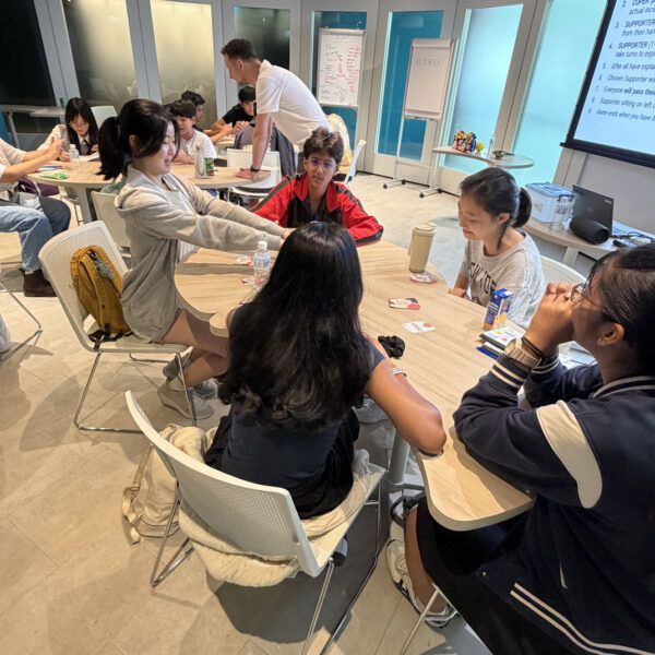 Students sit around a table, engaged in a group activity with cards in a modern classroom setting