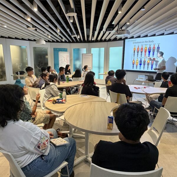 A presenter points to a slide titled Emotions in the Body during a workshop with a group of students