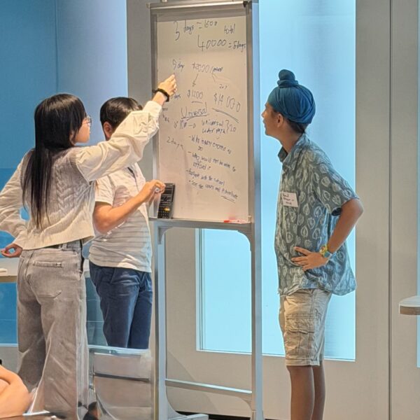 Three people collaborating and pointing at notes on a whiteboard in Youth Leadership and Communication camp