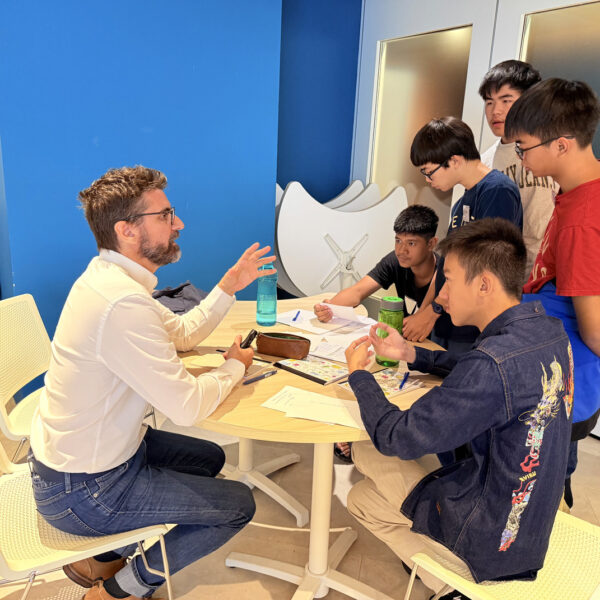 A mentor gestures while speaking to a group of students gathered around a table for a discussion