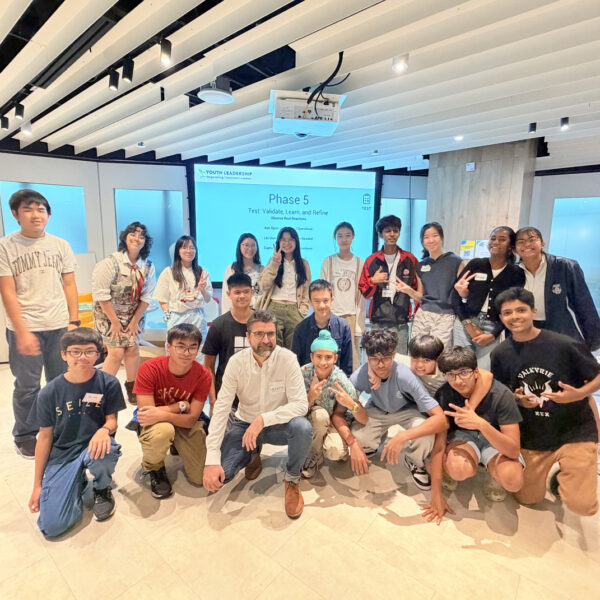 A group of diverse youth and a mentor posing in front of a Youth Leadership workshop presentation screen