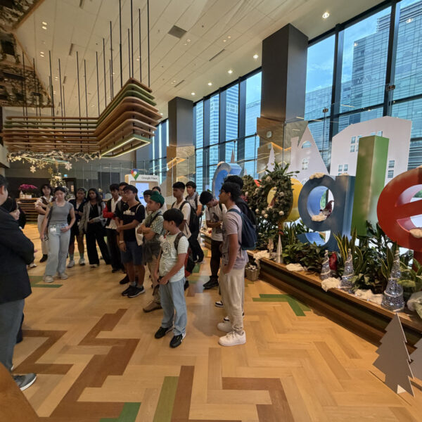 A group of students on a tour listening to a guide in a Google office lobby with a large Google sign