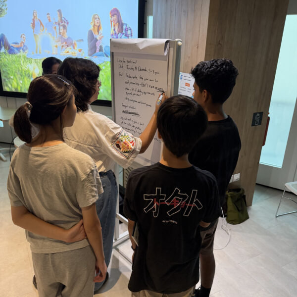 Four young people brainstorming and writing event details on a flip chart in Youth Leadership and Communication Camp