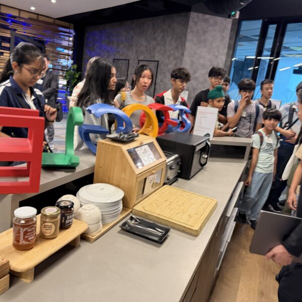 A group of students on a tour of a Google office, gathered around a snack counter with large Google letters