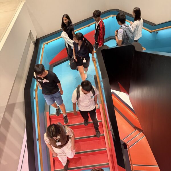 Students walking on a modern staircase with red steps and blue walls, viewed from a high angle