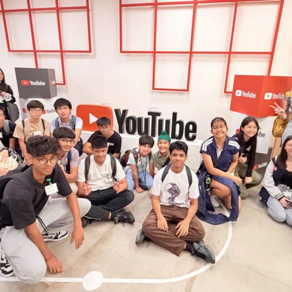 A group of diverse teenagers posing for a photo in front of a large YouTube logo