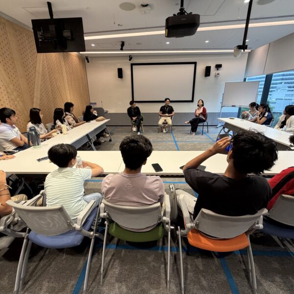 A group of students in a seminar room listening to a panel of three speakers