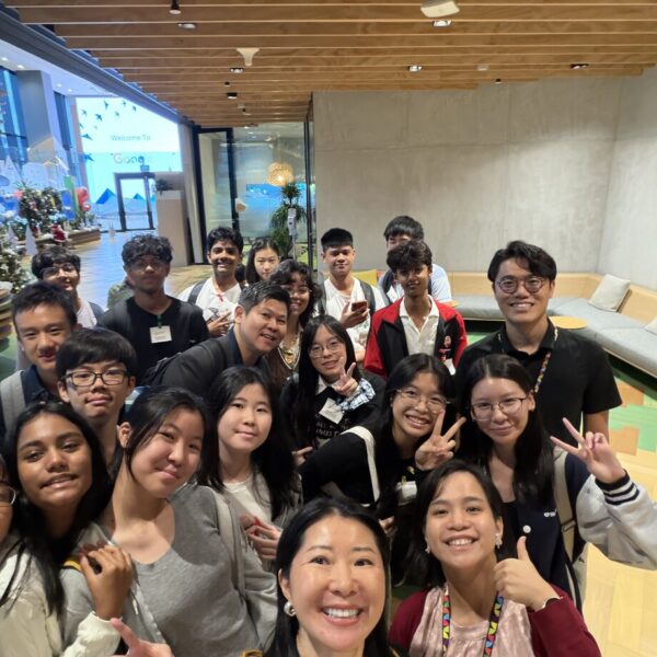A group of students and adults smiling for a photo in a Google office lobby