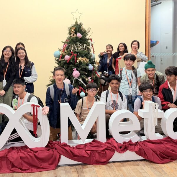 A group of young people posing around a large white Meta logo and a decorated Christmas tree