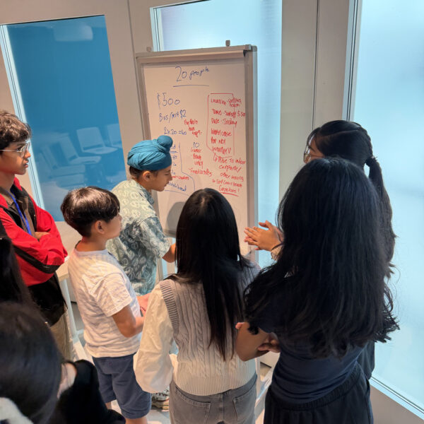 A group of young people brainstorm and collaborate on event planning notes on a whiteboard at Youth Leadership and Communication Camp