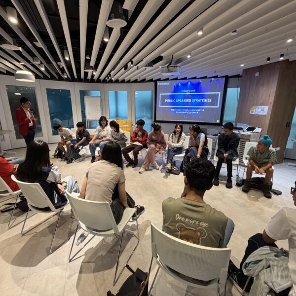 Students in a circle for a Public Speaking Strategies workshop led by a presenter in a red jacket