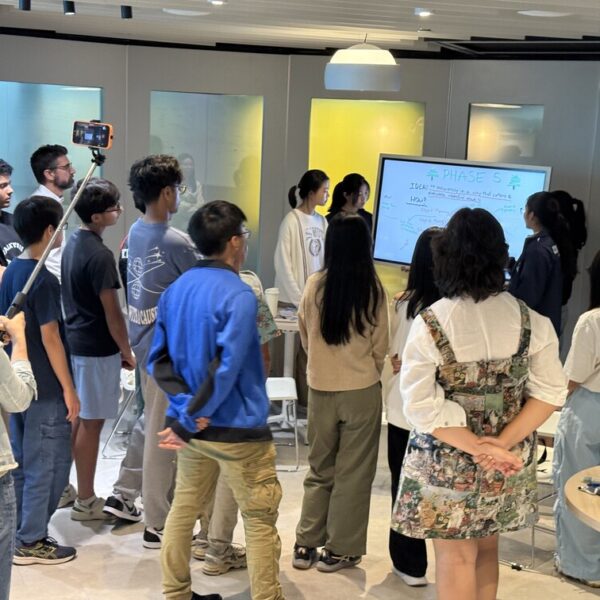A group of students gathered around a digital whiteboard for a presentation titled Phase 5