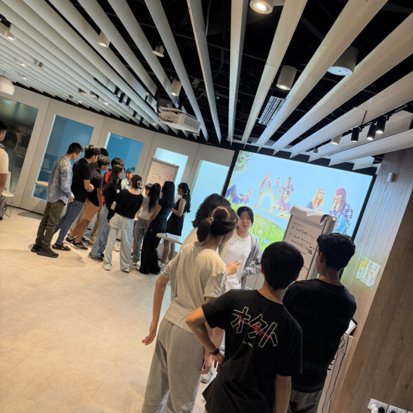 Students collaborating in small groups around whiteboards in a modern workshop space at Youth Leadership and Communication Camp
