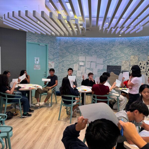 Students participating in a workshop, holding up papers and collaborating at tables in a modern classroom at Youth Leadership and Communication Camp