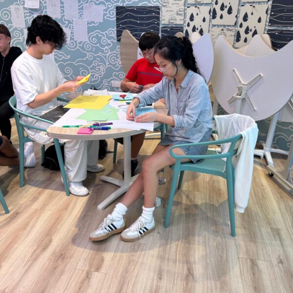 Four students sitting around a table working on paper crafts with colored paper and markers in Youth Leadership and Communication Camp