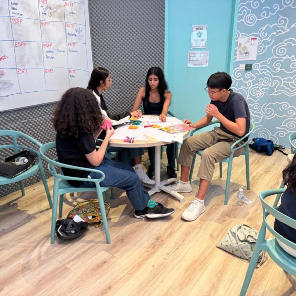 Four students collaborate on a project at a round table in a creative workspace at Youth Leadership and Communication Camp