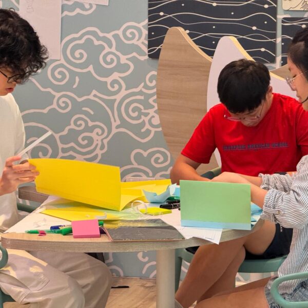 Three students at work together on a colorful paper craft project for Youth Leadership and Communication Camp