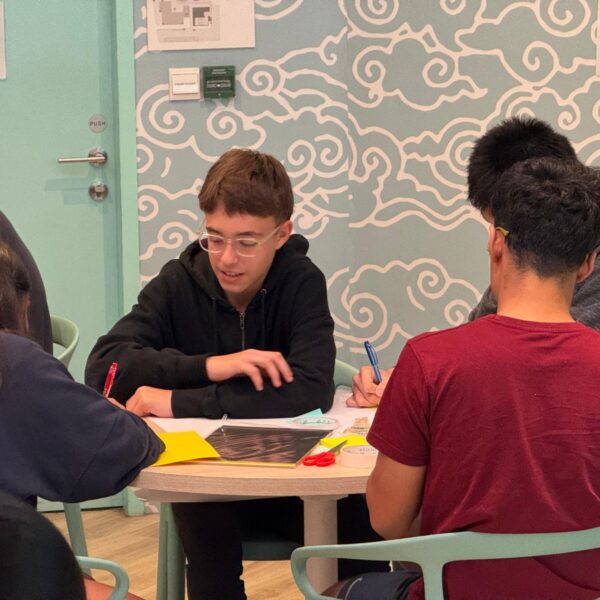 Students collaborating on a project at a round table with papers and craft supplies at Youth Leadership and Communication Camp