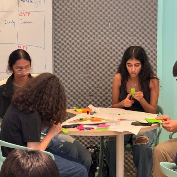 Four students sitting around a table collaborating on a hands-on project with paper and craft supplies in Youth Leadership and Communication Camp