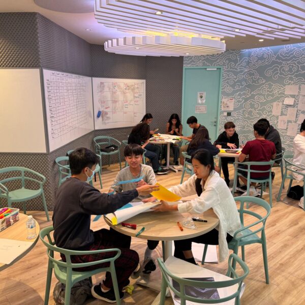 Students collaborating on creative projects at round tables in a modern workshop space at Youth Leadership and Communication Camp