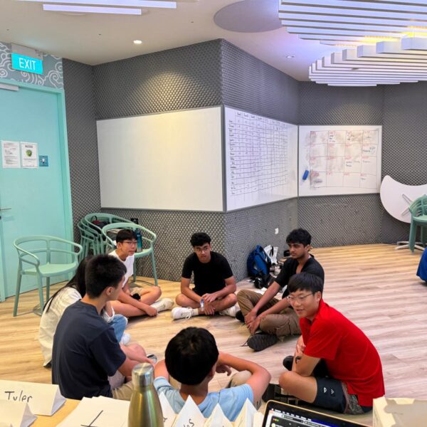 A group of young people sitting in a circle on the floor of a modern room, engaged in a discussion in Youth Leadership and Communication Camp