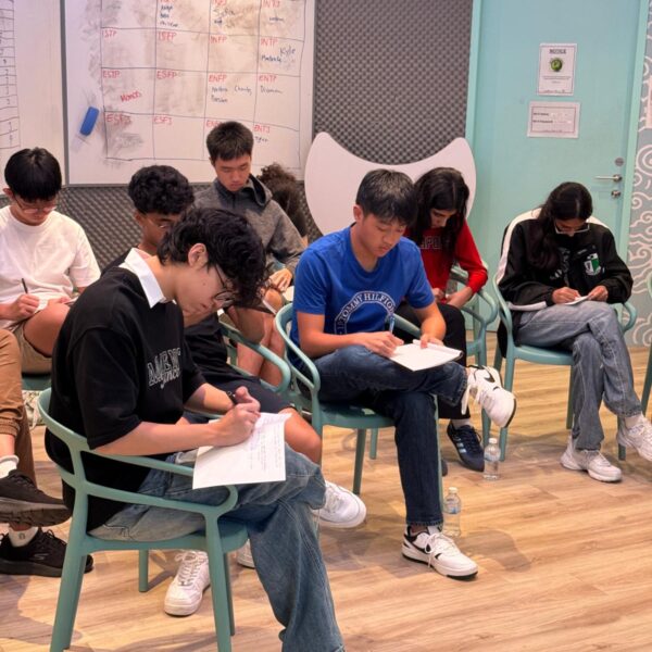 A group of students sitting in a circle and writing in notebooks in front of a personality types whiteboard in Youth Leadership and Communication camp