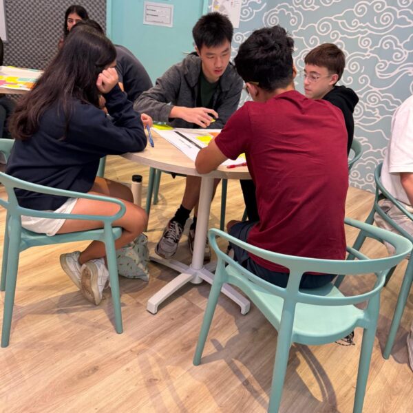 Four students sit around a table collaborating on a project with papers and sticky notes in Youth Leadership and Communication Camp